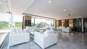 A spacious lobby with white sofas, a glass coffee table, and a large TV screen. - B2 Korat Premier Hotel (Nakhon Ratchasima)