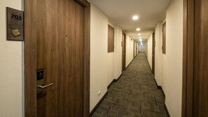 A hotel hallway with wooden doors, carpeted floors, and a number sign on the wall. - B2 Korat Premier Hotel (Nakhon Ratchasima)