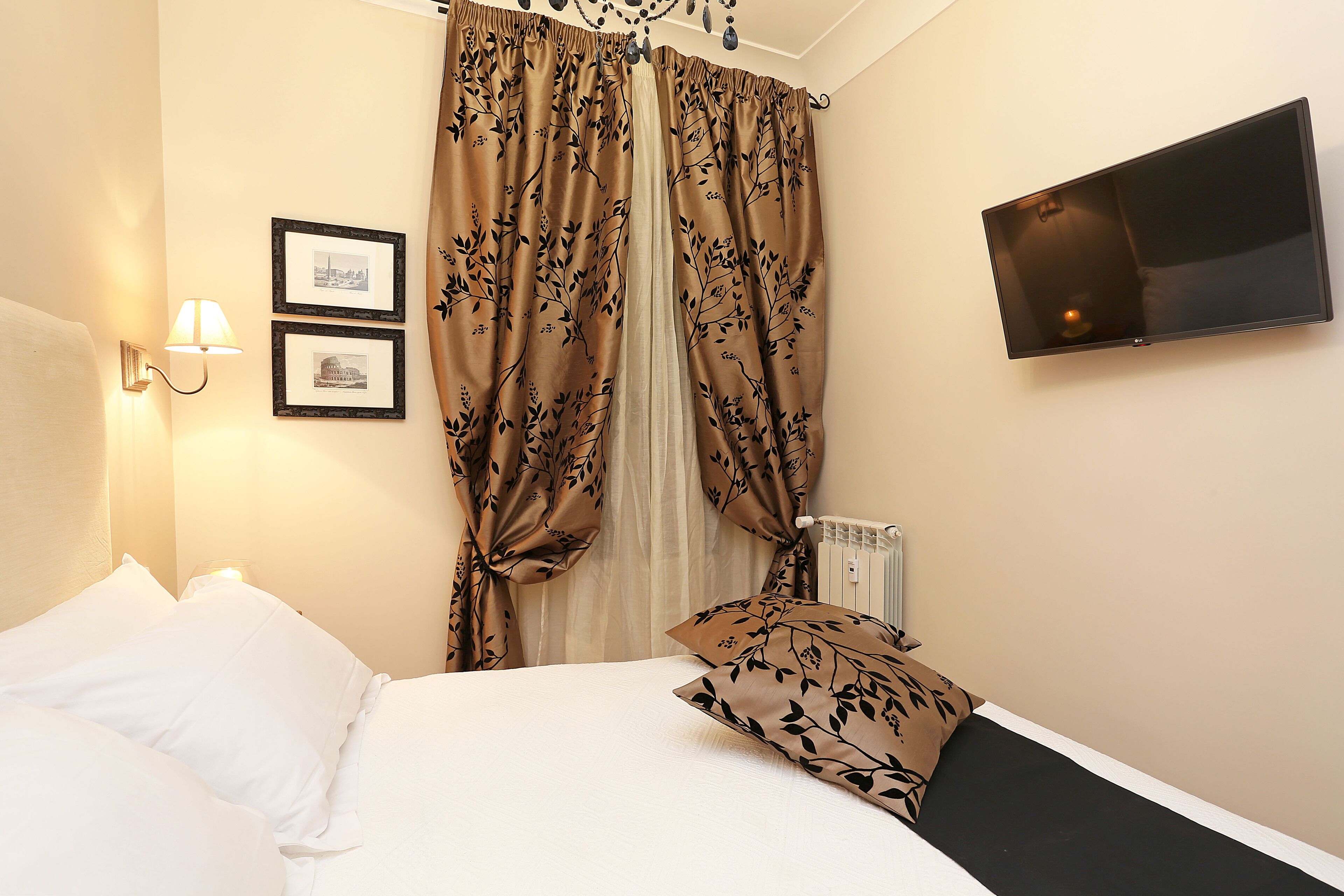 Habitación de hotel con una cama, televisor de pared y ventana con cortinas.