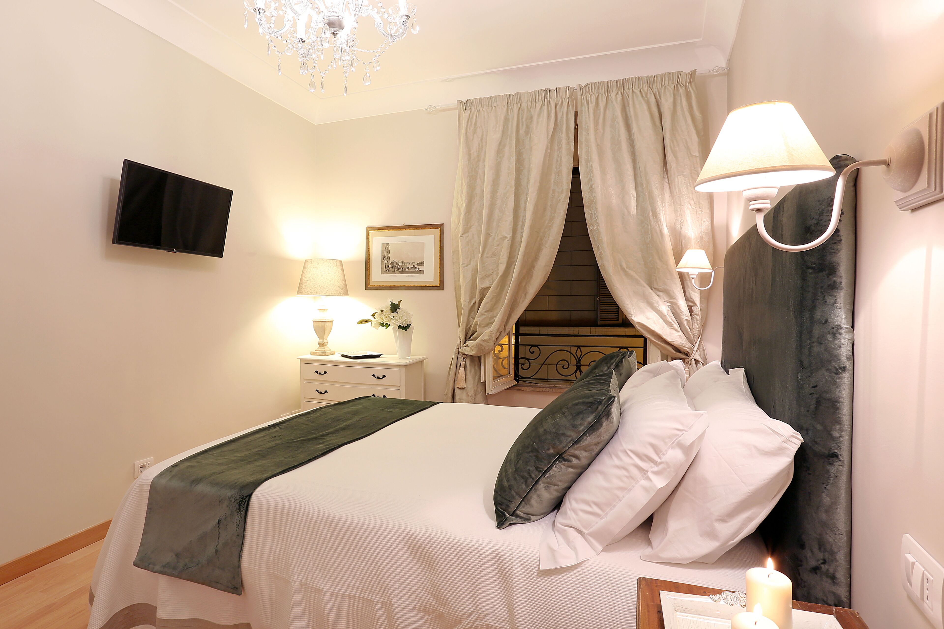 A bedroom with a bed, bedside lamps, a TV, a picture on the wall, and a chandelier.