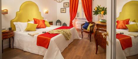 A hotel room with two beds, each with a yellow headboard, white bedding, and red accents. There is a wooden nightstand with a lamp, a wooden chair, and a small table with a vase of flowers.