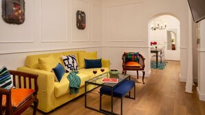 A living room with a yellow sofa, a glass coffee table, and a wooden chair. - Daplace - Flaminia Apartment (Rome)