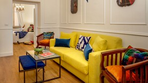 A living room with a yellow sofa, a glass coffee table, and a wooden chair. - Daplace - Flaminia Apartment (Rome)