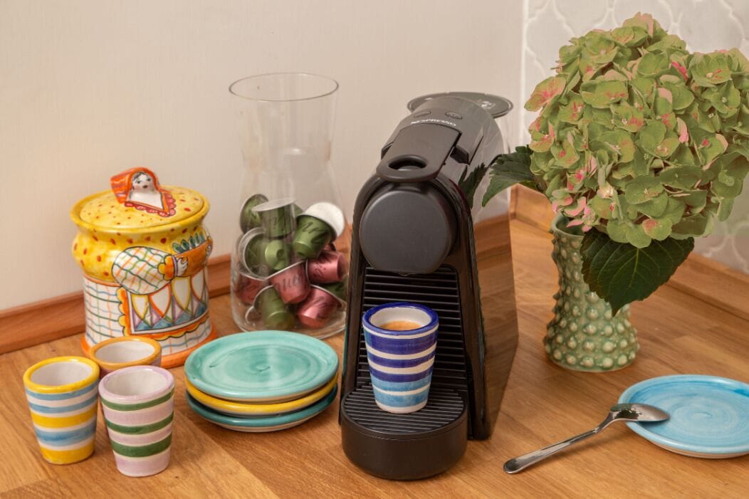 A kitchen setup with a coffee maker, various cups, a jar, and a potted plant.
