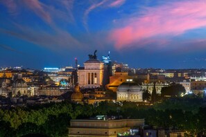A cityscape at dusk with illuminated buildings and a prominent dome structure. - Daplace - Terenzia Apartment (Rome)