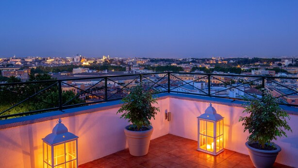 A rooftop terrace with potted plants and lanterns, overlooking a cityscape at dusk. - Daplace - Terenzia Apartment (Rome)