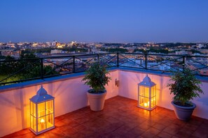 A rooftop terrace with potted plants and lanterns, overlooking a cityscape at dusk. - Daplace - Terenzia Apartment (Rome)