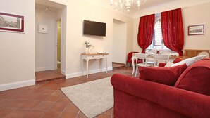 A living room with a red sofa, a white rug, a TV mounted on the wall, and a dining area with a table and chairs. - Daplace - Gaia Apartment (Rome)