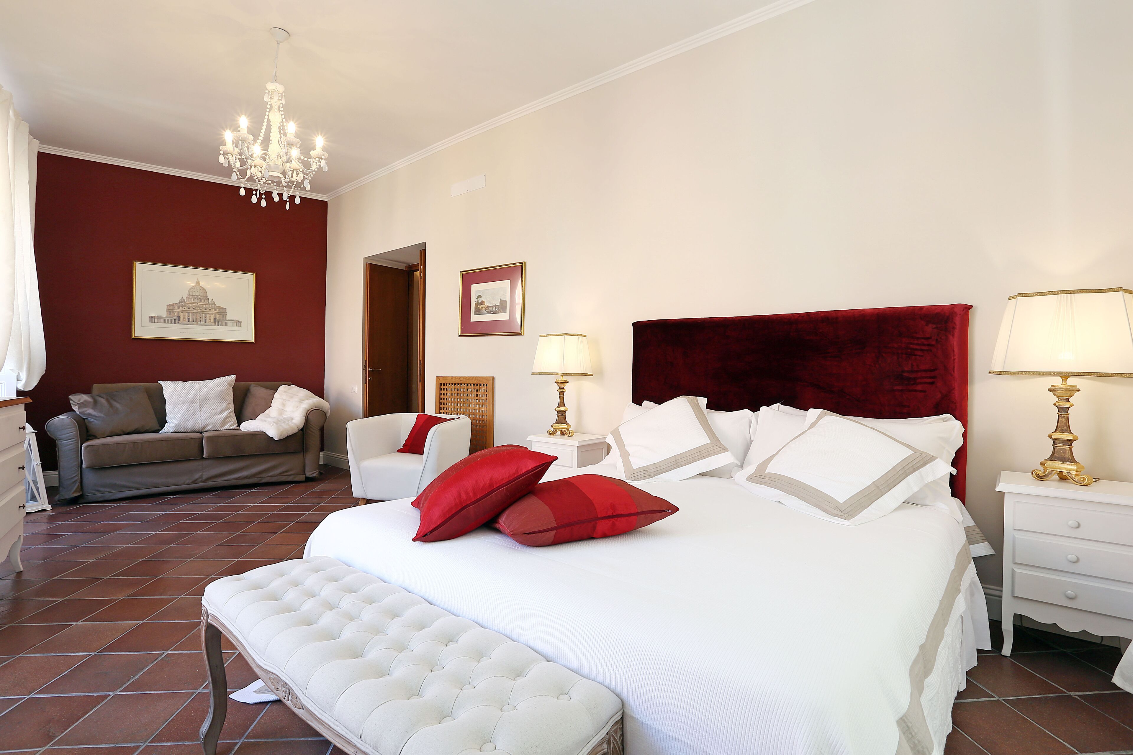 Un dormitorio ordenado con una cama grande, una zona de estar con sofá y sillones, y una araña.