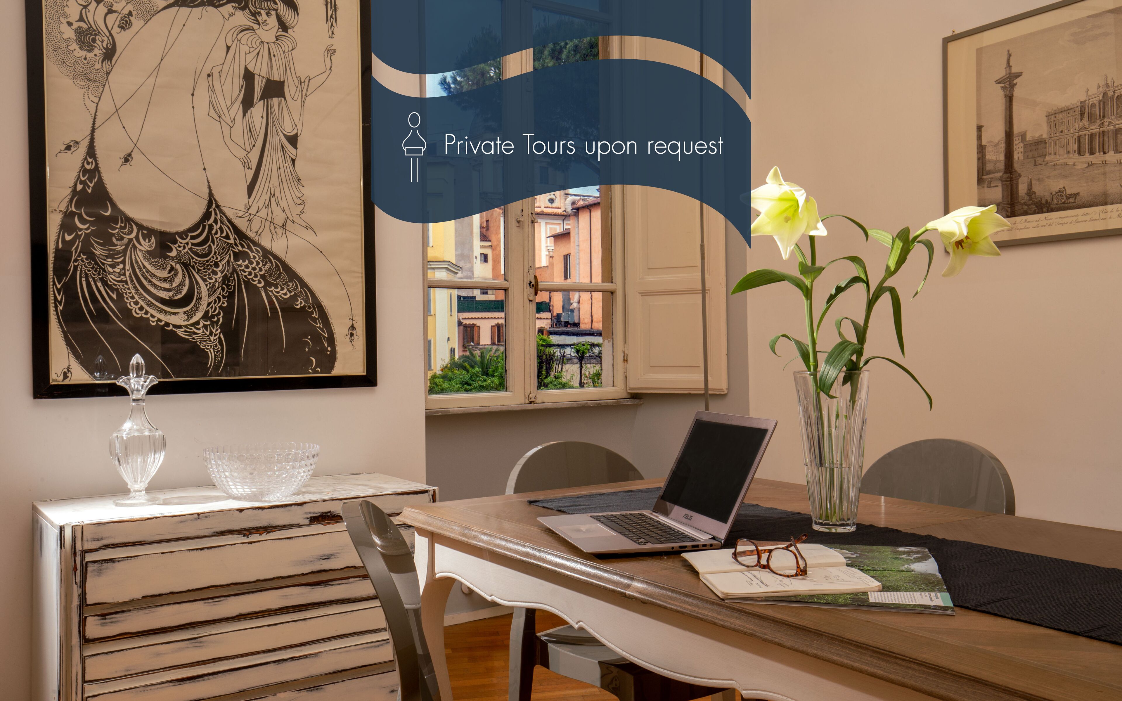 Een eethoek met een laptop, een vaas met bloemen en een lijst met een kunstwerk aan de muur.