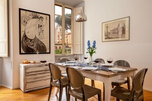 A dining area with a wooden table set for four, a white cabinet with drawers, and two framed artworks on the walls. - Daplace - Virginia Apartment (Rome)