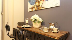A dining area with a wooden table, chairs, a vase with flowers, a candle, a pitcher, and a painting on the wall. - Daplace - Lucrezia Apartment (Rome)