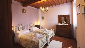 A bedroom with two beds, a wooden ceiling, a chandelier, a dresser, and a mirror. - Arcobaleno (Loro Ciuffenna)