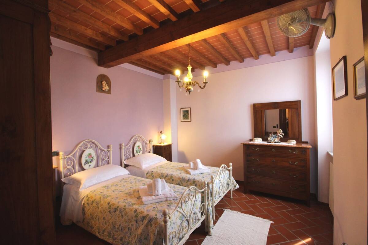 A bedroom with two beds, a wooden ceiling, a chandelier, a dresser, and a mirror.