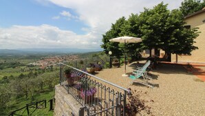 A terrace with a view of a valley, a pergola with a white umbrella, and outdoor seating. - Arcobaleno (Loro Ciuffenna)