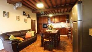 A living room with a leather sofa, a dining table with chairs, wooden cabinets, and a kitchen area with a refrigerator.