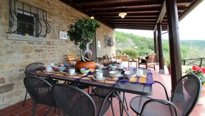 An outdoor patio with stone walls, a table set with bowls and cups, and a potted tree.