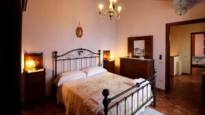 A bedroom with a four-poster bed, wooden headboard, a chandelier, a bedside table with a lamp, and a dresser with a mirror.