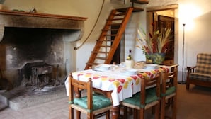 A dining area with a fireplace, wooden chairs, a table set for two, and a wooden staircase.