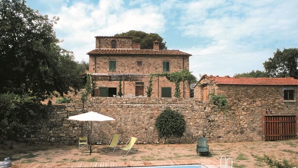 A stone building with a pool, a white umbrella, and two lounge chairs.