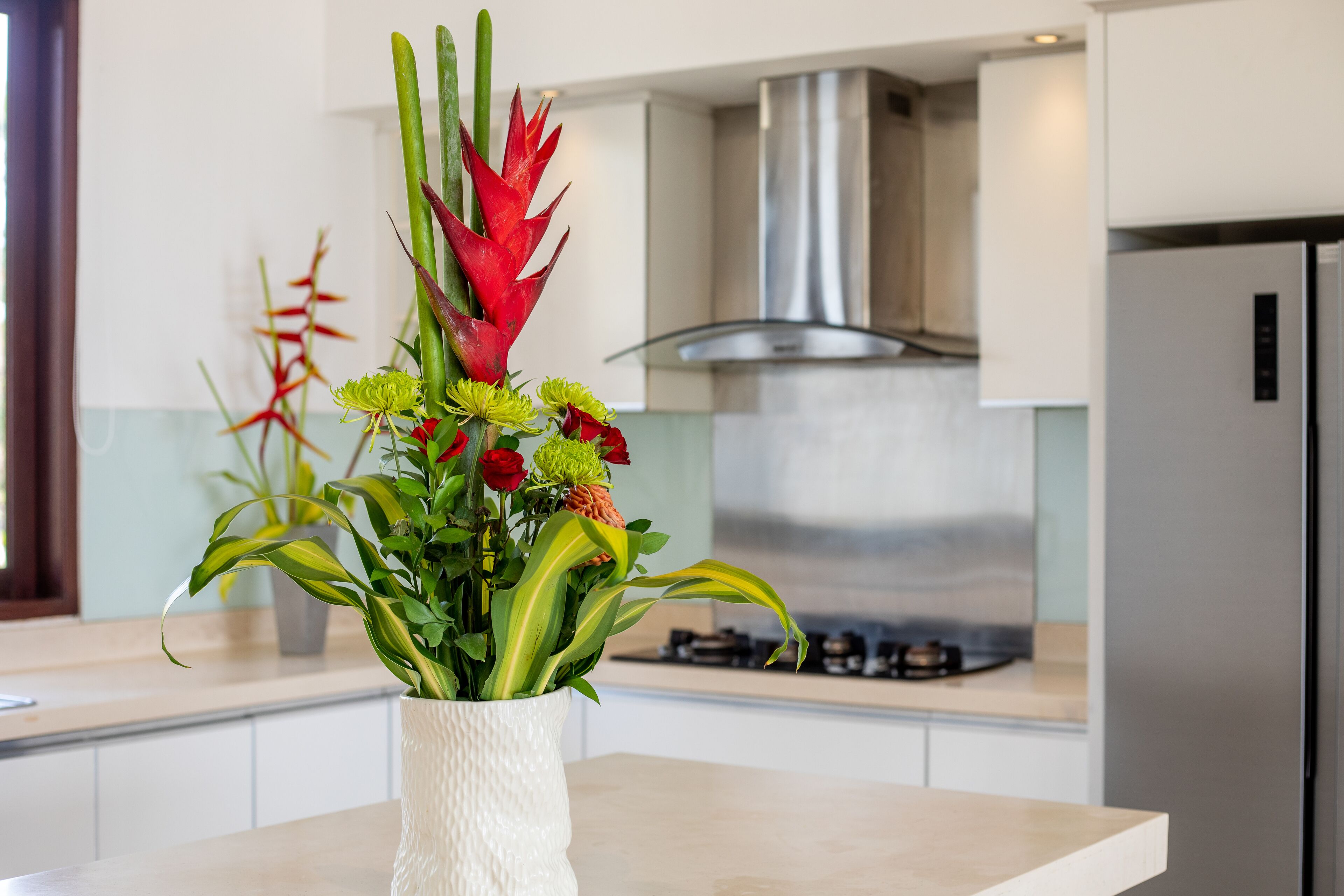 A modern kitchen with a white vase containing red and green flowers on the counter.