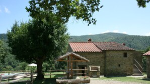 Edifici de pedra rústic amb teulada a dues aigües, envoltat per una tanca de fusta i un arbre gran.