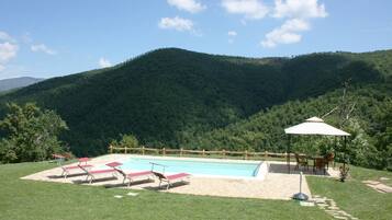 Relax by the pool surrounded by lush green hills and a shaded gazebo.