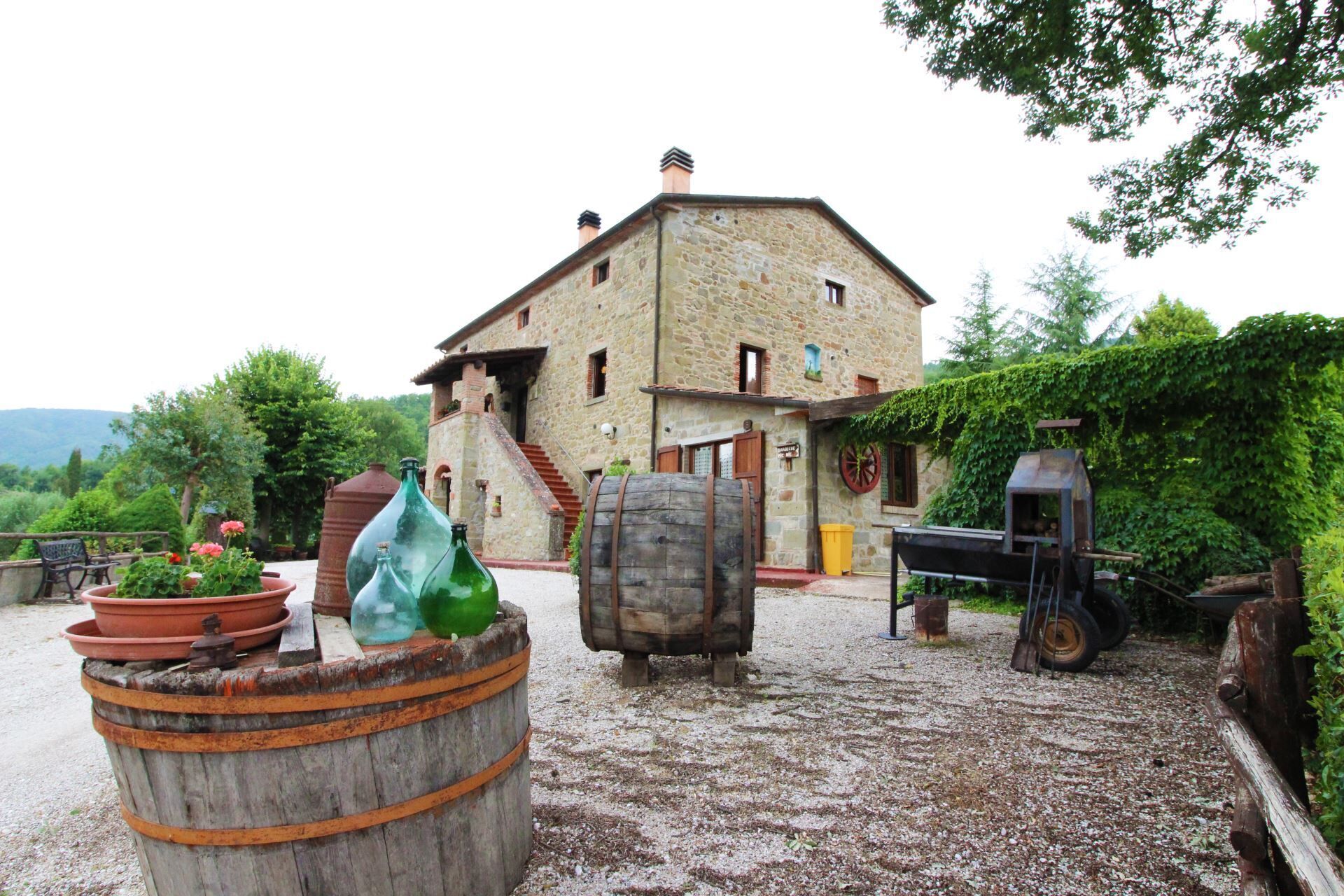 A rustic stone building with a sloped roof, surrounded by greenery and a gravel path.