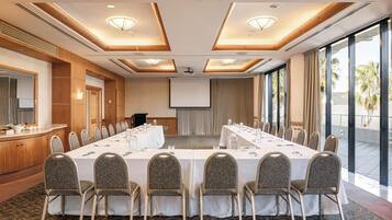 Uma sala de conferências com uma mesa comprida, cadeiras, uma tela de projetor e uma janela grande.