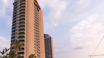 Un edificio alto y moderno con varios balcones, rodeado de palmeras y un cielo despejado.