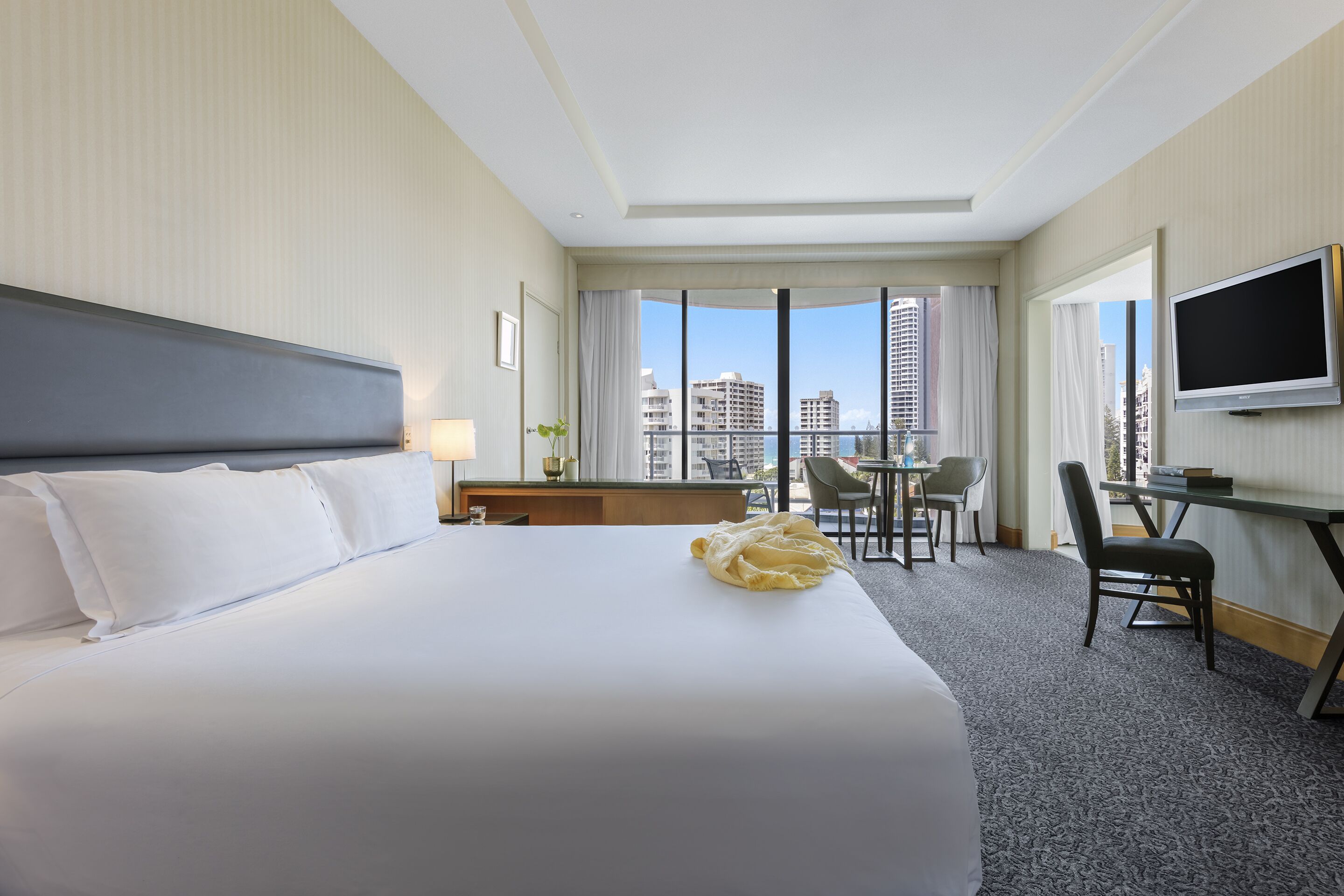 Habitación de hotel con una cama grande, un escritorio, una silla, un televisor y vistas a la ciudad.