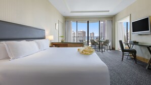 Ein Hotelzimmer mit einem großen Bett, einem Schreibtisch, einem Stuhl, einem Fernseher und Blick auf die Stadt.