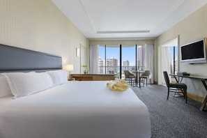 A hotel room with a large bed, a desk, a chair, a TV, and a view of the city.