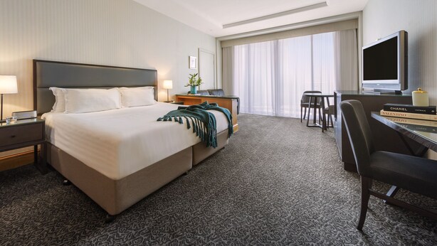Ein Hotelzimmer mit einem großen Bett, einem Schreibtisch mit Fernseher und einem Fenster mit Vorhängen.
