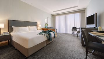 A hotel room with a large bed, a desk with a TV, and a window with curtains.