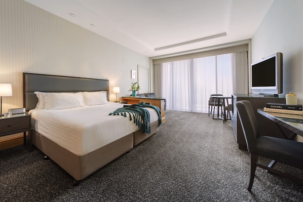 A hotel room with a large bed, a desk with a TV, and a window with curtains.