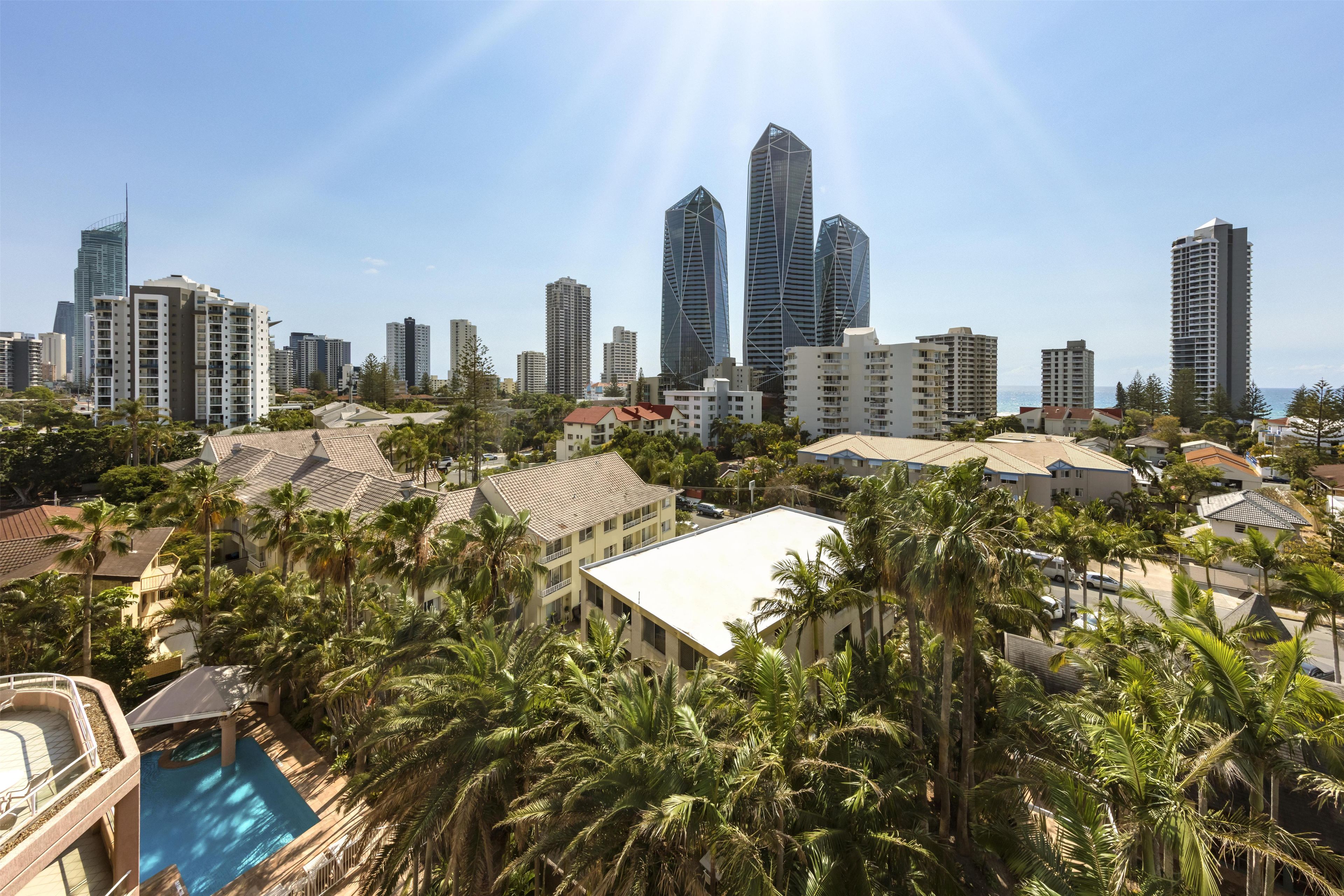 A residential area with a pool, palm trees, and a city skyline with tall buildings.