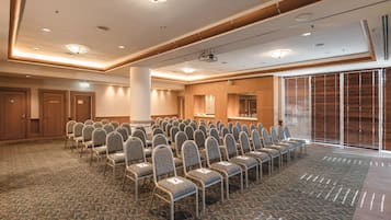 A conference room with rows of chairs, a stage with a projector, and a large window with blinds.