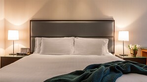 Ein ordentlich bezogenes Bett mit weißer Bettwäsche und einem dunklen Kopfteil, flankiert von zwei Nachttischen mit Lampen und einer Blumenvase.
