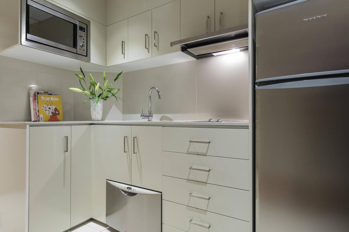 A modern kitchen with white cabinets, a stainless steel refrigerator, a microwave, and a sink with a faucet.