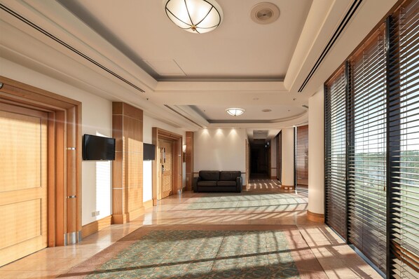 A modern hotel corridor with wooden doors, a flat-screen TV, a sofa, and large windows with blinds. - Oaks Gold Coast Hotel (Surfers Paradise)