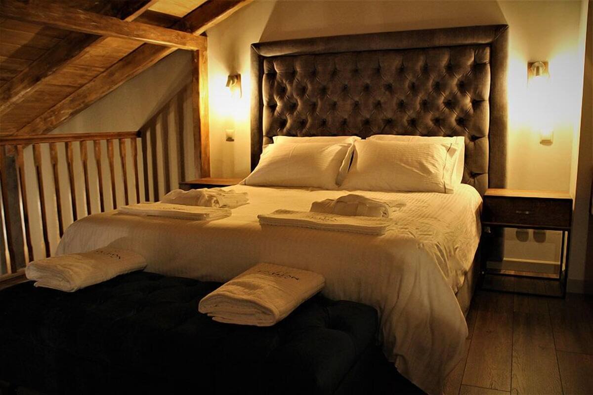 Een keurig opgemaakt bed met kussens en opgevouwen handdoeken, een houten hoofdbord en een nachtkastje met een lamp.