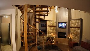 A cozy living room with a spiral staircase, a stone fireplace, and a television mounted on the wall. - Mylaon Boutique Hotel & Spa (Gortynia)