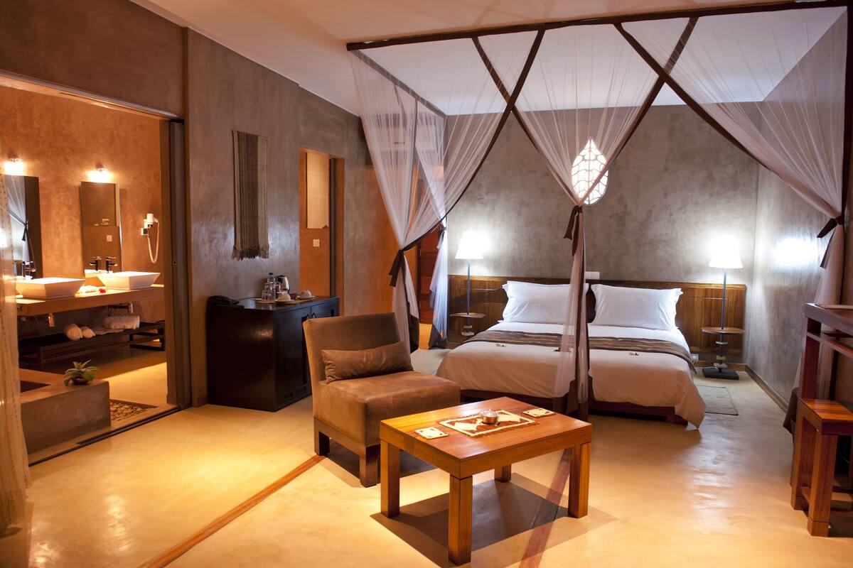 A bedroom with a canopy bed, a sitting area with a table, and a bathroom with a sink and mirror.