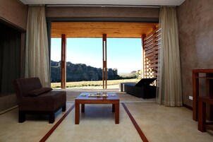 Una sala de estar moderna con un gran ventanal corredero, una mesa de madera, un sofá marrón y un sillón negro.