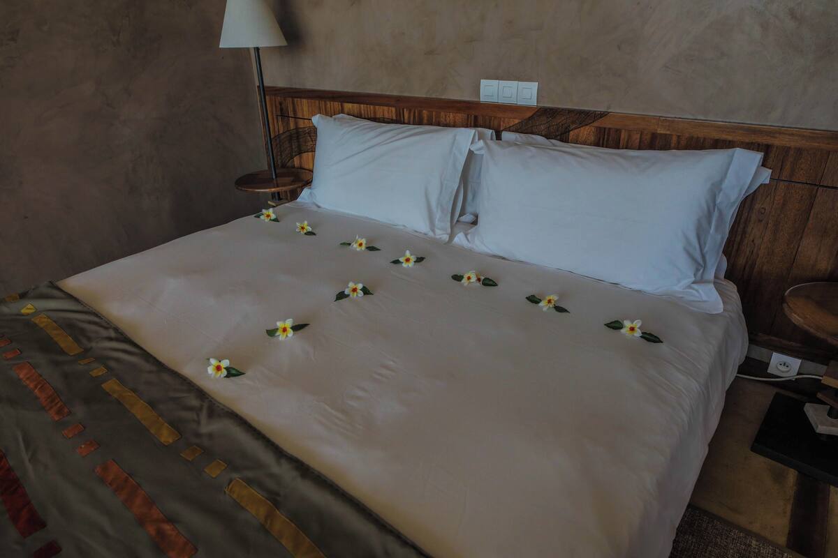 A neatly made bed with white linens and small white flowers, a wooden headboard, and a bedside table with a lamp.
