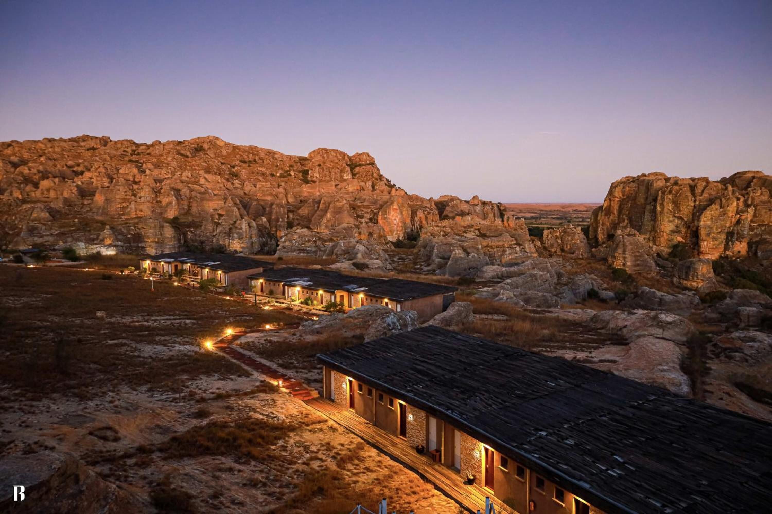 A rustic building with multiple rooms, surrounded by rocky terrain and a clear sky.