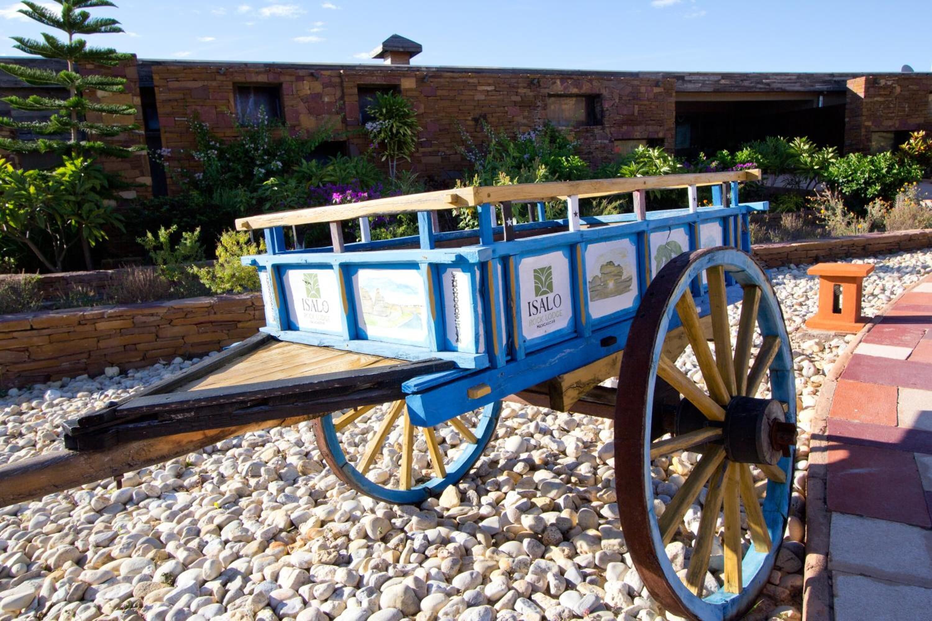 A blue cart with 'ISALO' branding, parked on a gravel path with a brick building in the background.