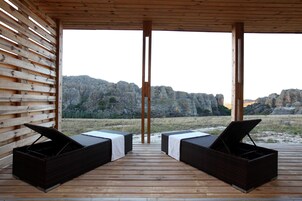 Una terraza de madera con dos sillones de mimbre mirando a un paisaje rocoso.