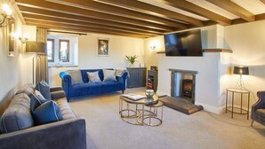 A living room with a sofa, a coffee table, a fireplace, and a TV mounted on the wall. - Host & Stay | The Coach House (Whitby)